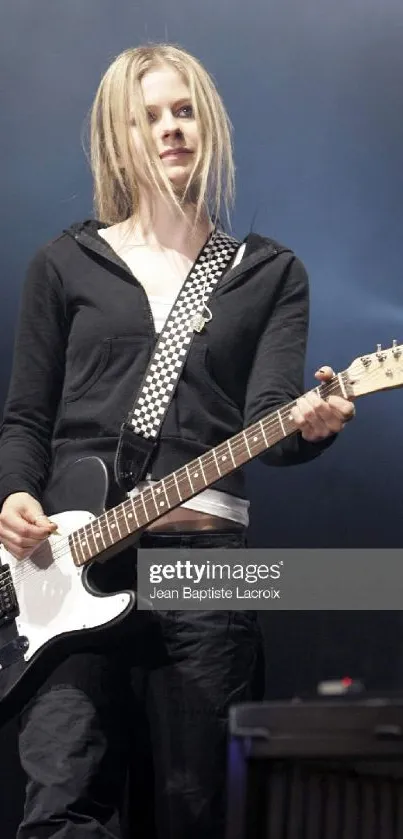 Guitarist performing live on stage with a checked strap and electric guitar.