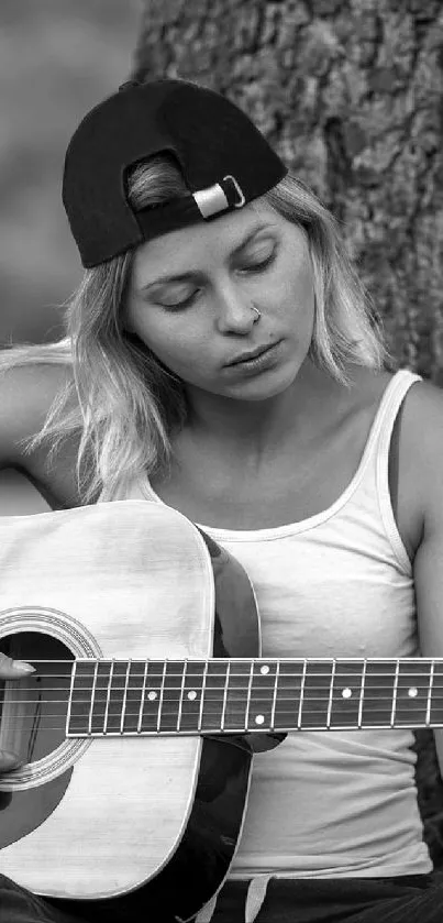 Woman playing guitar under a tree in black and white.