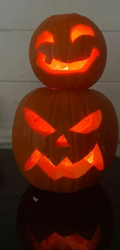 Carved Halloween pumpkins with glowing orange faces on a dark surface.