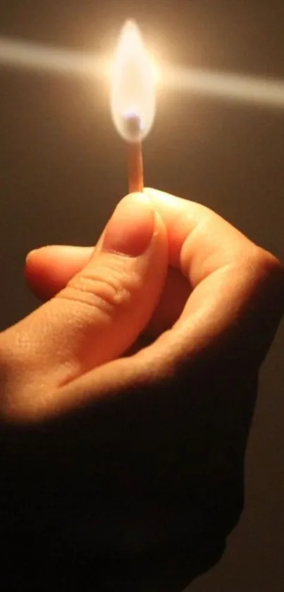 A hand gently holding a burning match in the dark background.