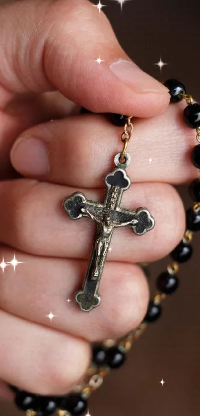 Close-up of a hand holding a black rosary with a cross.