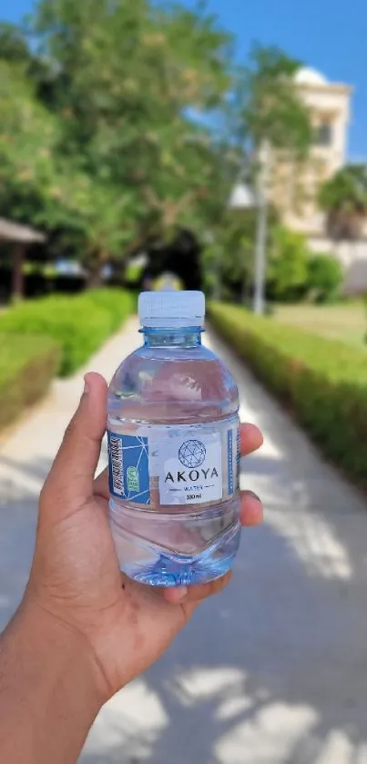 Person holding water bottle outdoors with trees and blue sky.