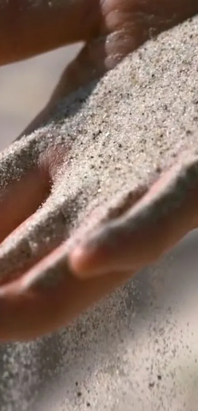 A close-up of a hand letting sand flow gently through fingers on a mobile wallpaper.