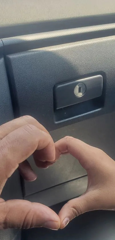 Two hands forming a heart shape against a car interior background.