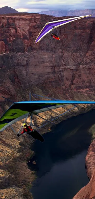 Two hang gliders soar over a picturesque river canyon.