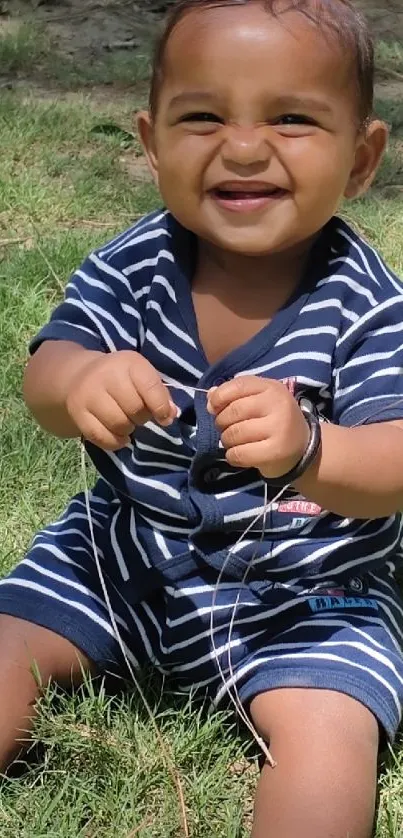 Smiling baby in striped outfit sitting on grass.