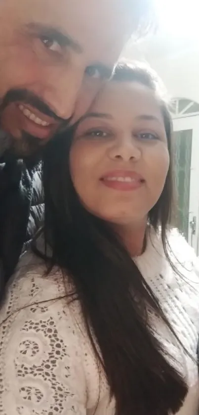 Cheerful couple taking a selfie indoors with a gift box in hand.