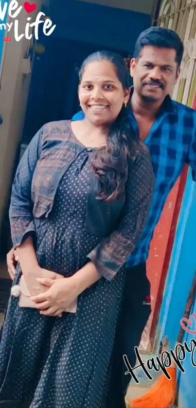 A happy couple stands smiling against a blue door background.