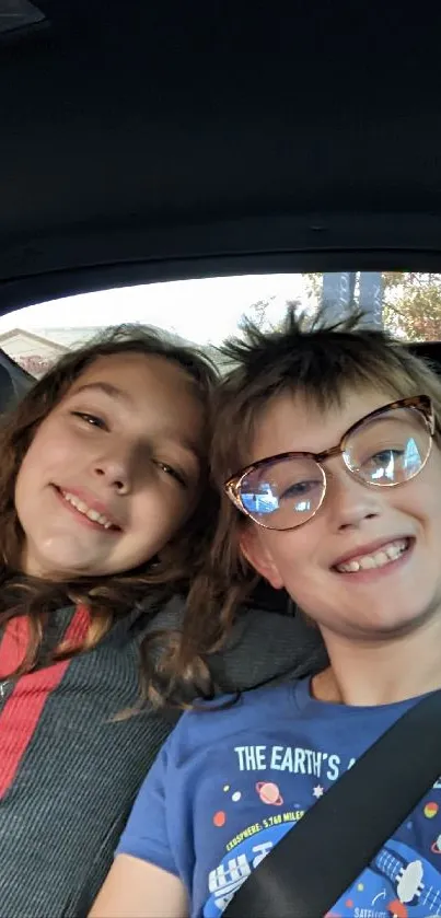 Two kids smiling and taking a selfie in a car backseat.