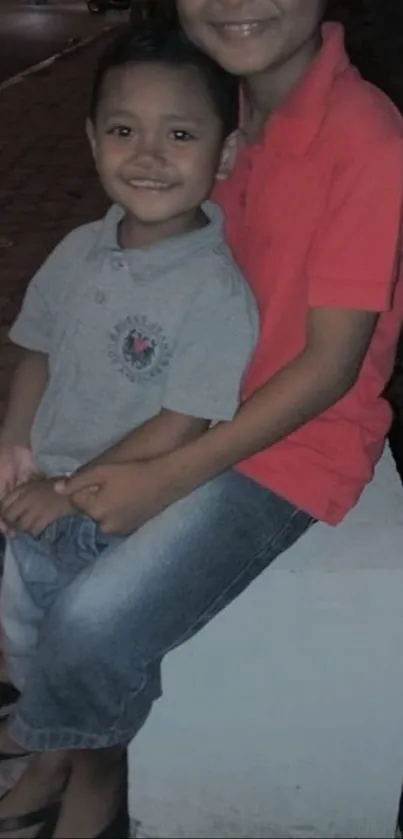 Two smiling children sitting together at night.