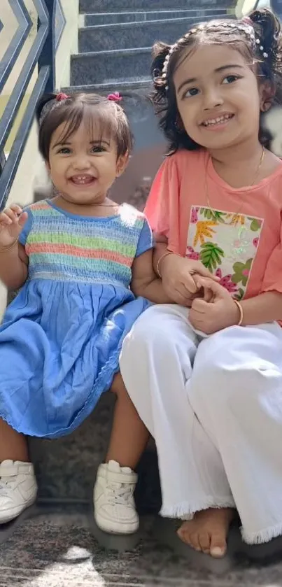 Two smiling children sitting on stairs in casual outfits.