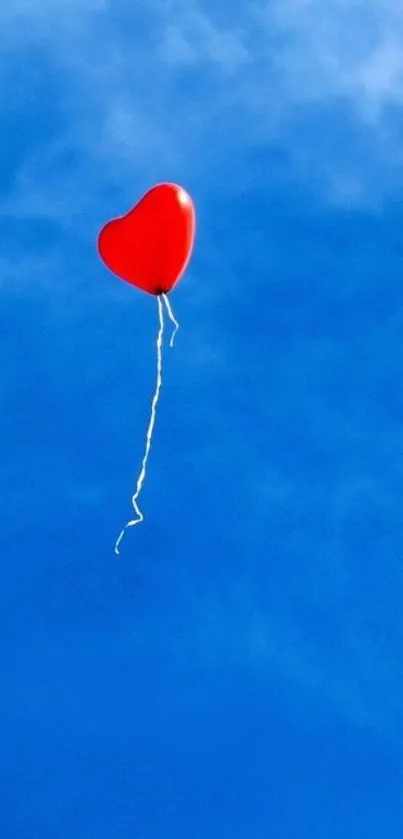 Red heart balloon floating in clear blue sky background.