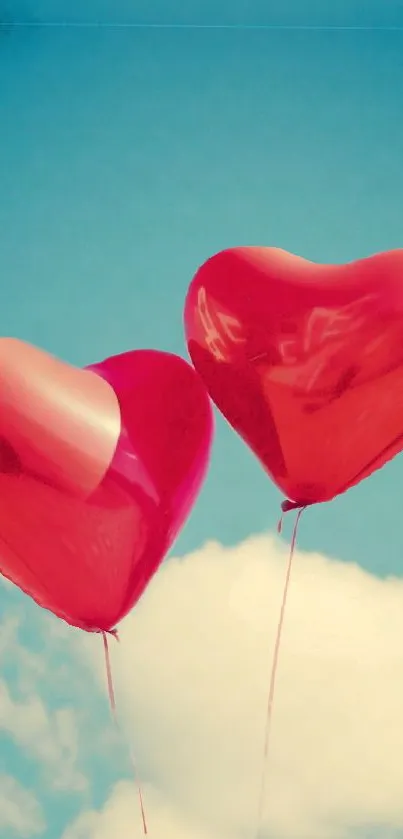 Two red heart balloons float in a blue sky with clouds.