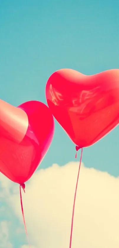 Two heart balloons float in a clear blue sky with fluffy clouds.