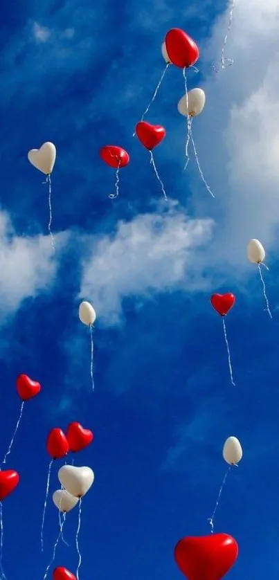 Red and white heart balloons floating in a clear blue sky with fluffy clouds.