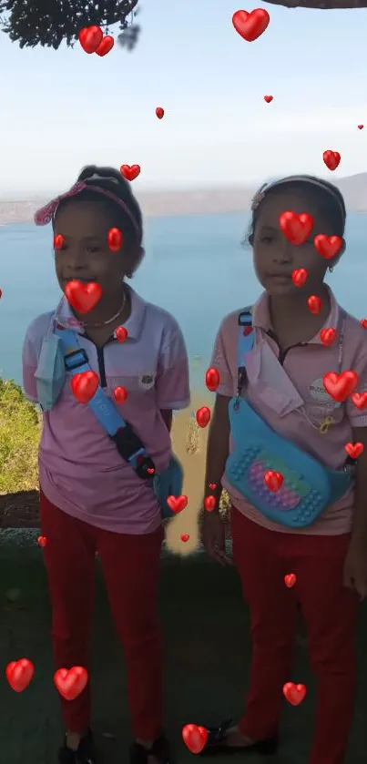 Two smiling children with hearts against a lakeside view.