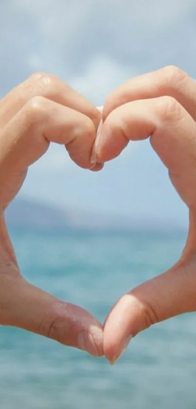 Hands forming a heart shape over a blue ocean background.