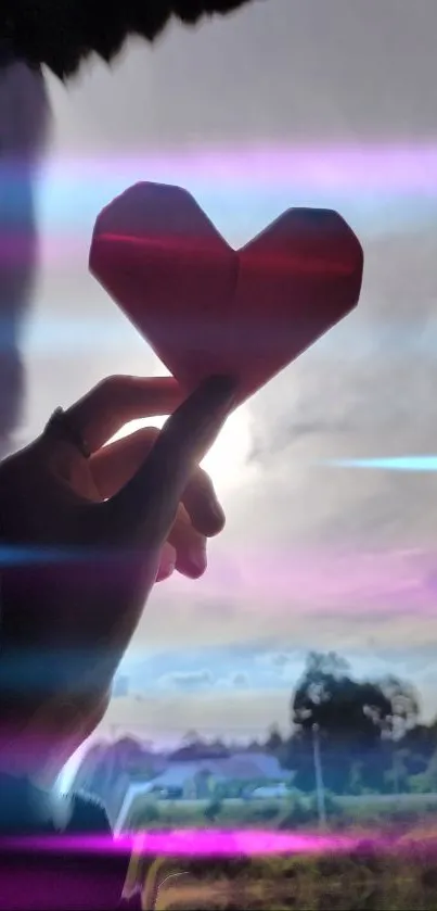 Hand holding origami heart with pink light streaks in a scenic setting.