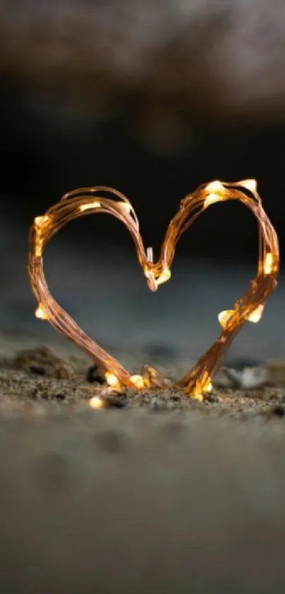 Glowing heart-shaped wire light on sandy beach background.