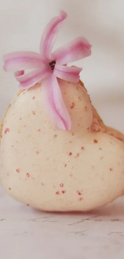 Heart-shaped macaron with pink flower embellishment on soft background.