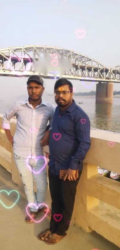 Two men stand by a bridge with heart overlays, creating a picturesque scene.