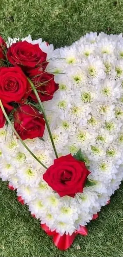 Heart-shaped floral arrangement with red roses on green grass.