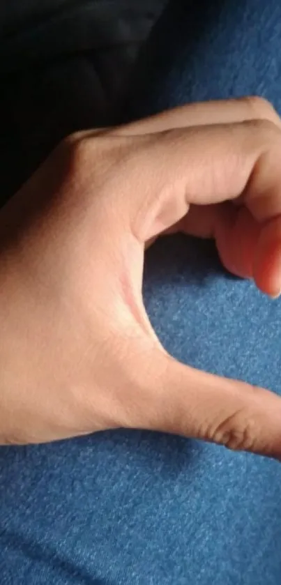 Hand forming a heart shape on blue fabric.