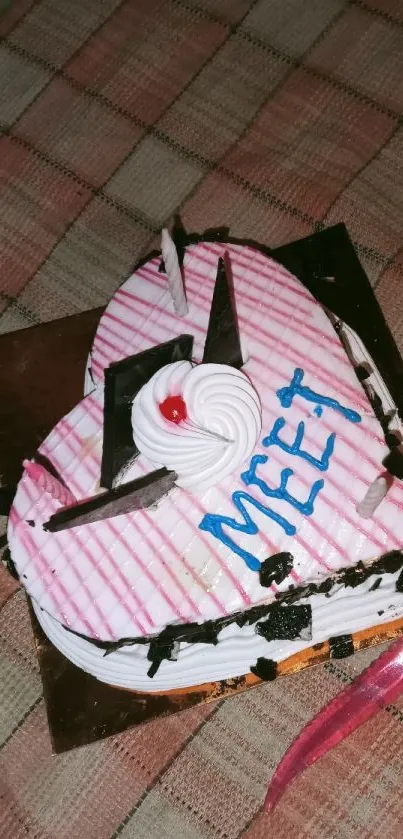 Heart-shaped cake with decorations on a plaid tablecloth.