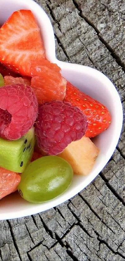 Heart-shaped bowls of mixed fresh fruit on wood.