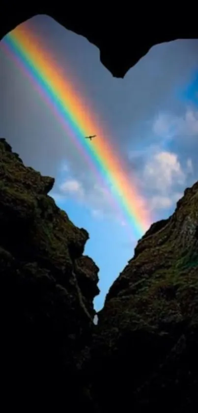 Rainbow through heart-shaped rock opening with bird in sky.