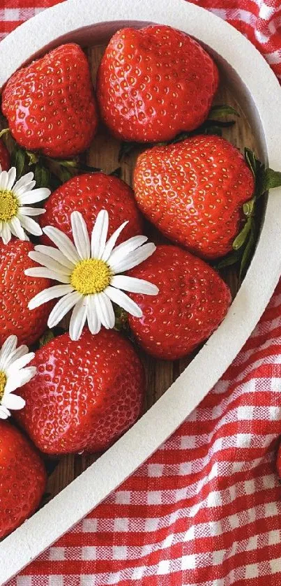Heart-shaped bowl of strawberries and daisies on red checkered cloth.
