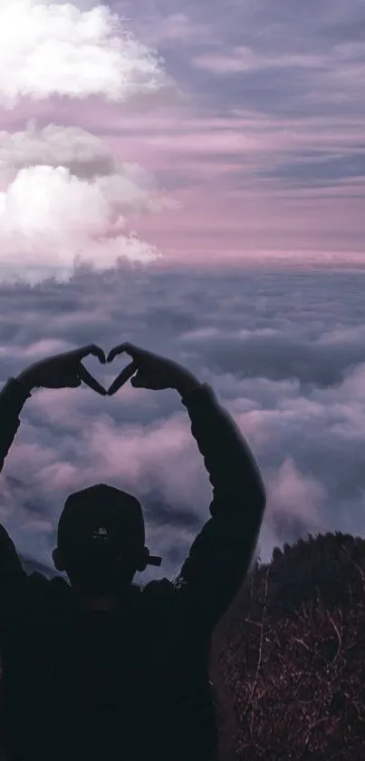 Silhouette making heart sign over pink cloud landscape.