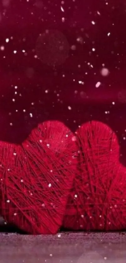 Two red yarn hearts in snowfall on maroon background.