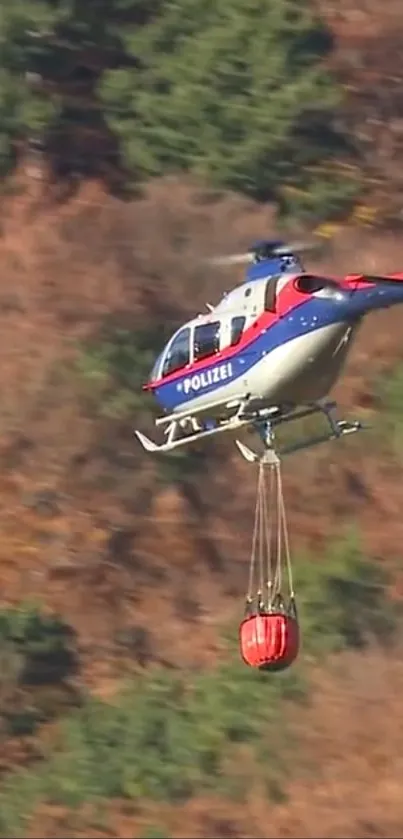 Police helicopter over autumn forest with firefighting bucket.