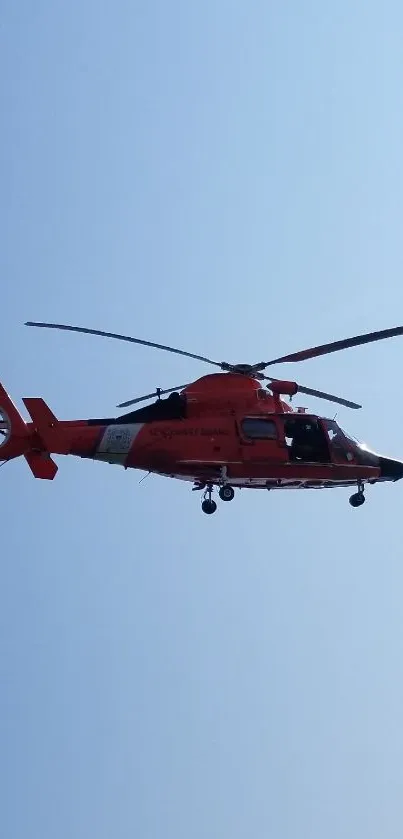 Red helicopter flying in a clear blue sky.