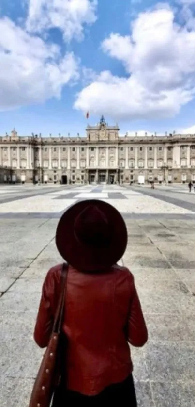 Person facing a historic building under a blue sky with clouds.