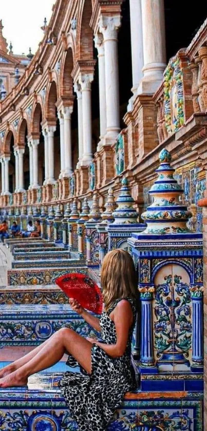 Woman sitting amidst Spanish architecture with a red fan.