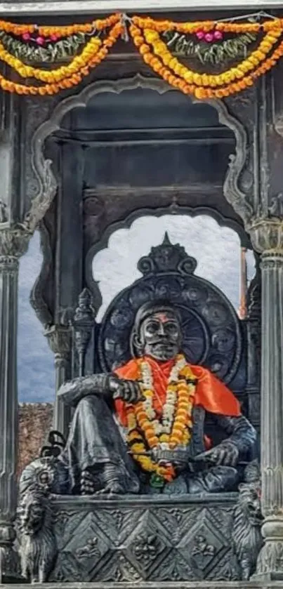 Historic statue with marigold garlands, set against a cloudy sky.