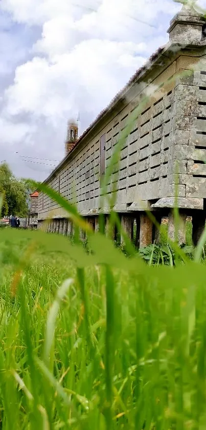 Historic stone building with lush green grass and cloudy sky.