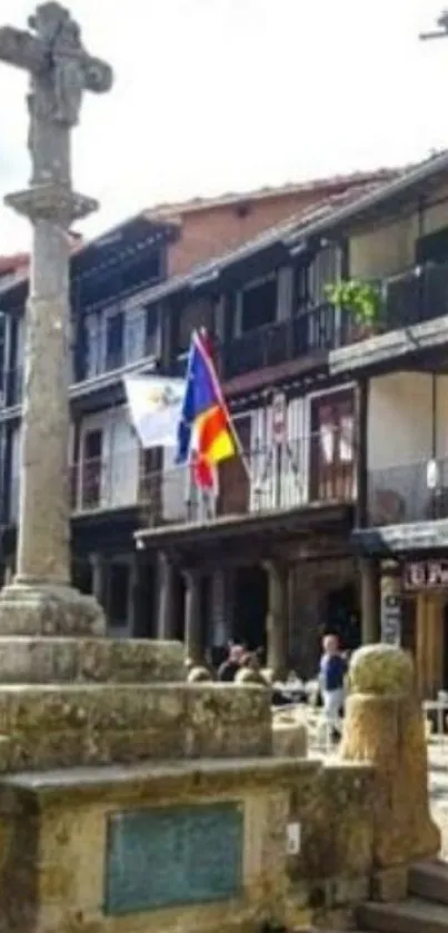 Historic stone cross in a vibrant town plaza with old buildings.