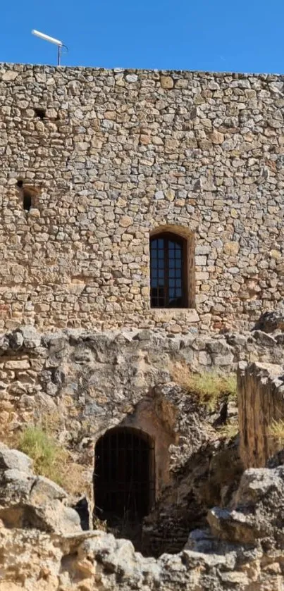 Historic stone wall under clear blue sky with window and ruins.