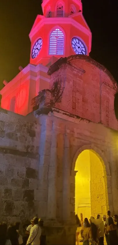 Historic tower illuminated at night with vibrant red and yellow lights.