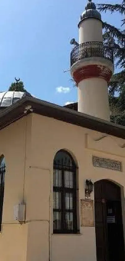 Historical mosque with minaret under a blue sky, surrounded by trees.