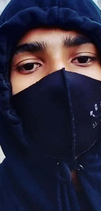 Hooded person wearing a black mask in an urban setting.