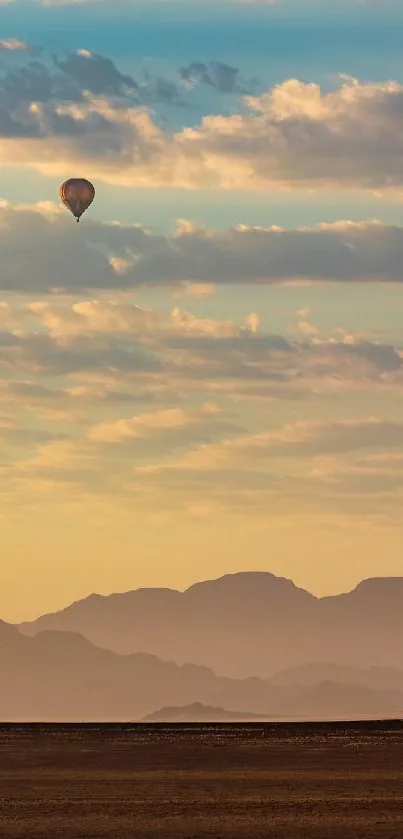 Hot air balloon floats over mountains at sunrise with a light blue sky.