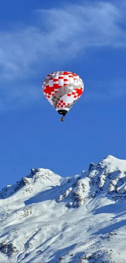 Vibrant hot air balloon over snowy mountain peaks under clear blue sky.