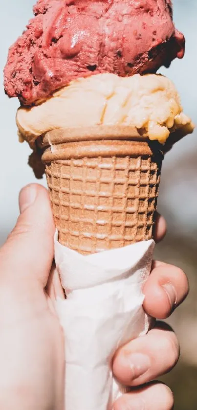 Hand holding a double scoop ice cream cone with pink and beige flavors.