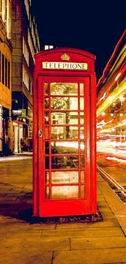 Red phone booth on a London street at night.