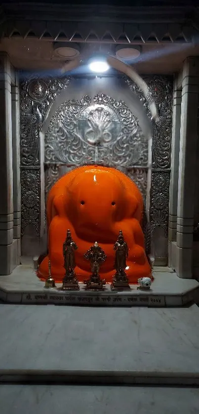 Orange Ganesh idol in a detailed temple setting, beautifully illuminated.