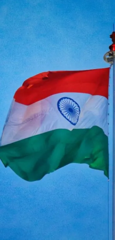 Indian flag waving in blue sky on a tall pole.